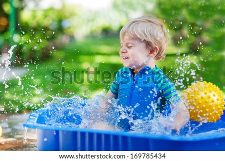 Little toddler boy having fun with splashing water in summer garden pool