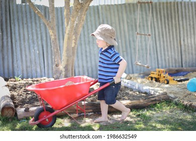 Little Toddler Boy Pushing Kid's Wheelbarrow. Backyard Sandpit Play.