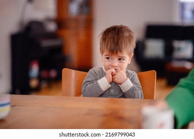 Little Toddler Boy Sitting At Wooden Table Sadly Looking Sideways