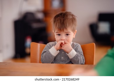 Little Toddler Boy Sitting At Wooden Table Sadly Looking Sideways