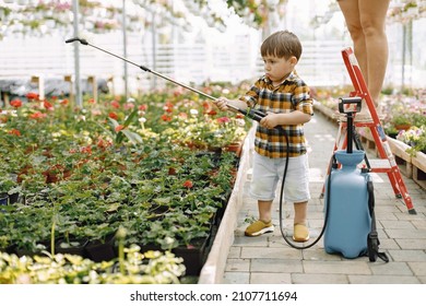 Little toddler boy watering flowers in a greengarden with water sprayer - Powered by Shutterstock