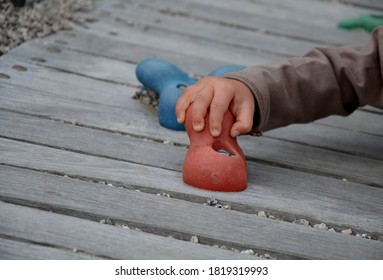 Little Toddler Child Climbs An Artificial Climbing Wall With Colorful Boulder Handles. Small Boy Hand Hold Colorful Stones On Wooden Board.