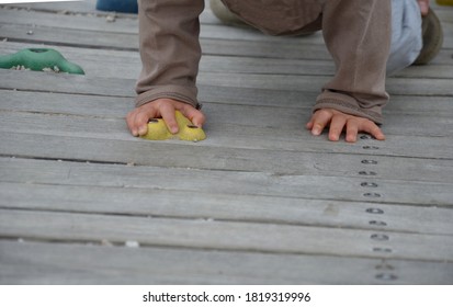 Little Toddler Child Climbs An Artificial Climbing Wall With Colorful Boulder Handles. Small Boy Hand Hold Colorful Stones On Wooden Board.