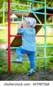 Little Toddler Climbing The Ladder Having Fun At Playground In Summer. Cute Young Boy, Kid Or Child Playing Outdoors On Playground. Stylish Little Baby Boy In Blue Shirt, Pants And Hat. Summer Time.