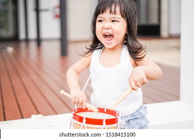 Little toddler drummer girl playing and hitting the drum set at home.Asian girl playing and singing happy moment in music lesson time.Child development and Executive function in child concept.