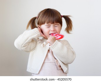 Little Toddler Girl Is Biting A Large Piece Of Hard Candy