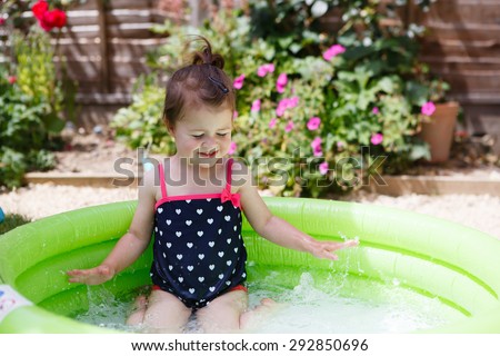 A little toddler girl in a black swimsuit playing in the pool in the garden