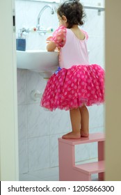 Little Toddler Girl In Dress Stand On Kids Wood Chair In Bathroom. Cute Child Washing Hand With Water And Soap.Prevent Flu: To Keep The Flu Virus At Bay, Wash Hands With Soap And Water Several Times