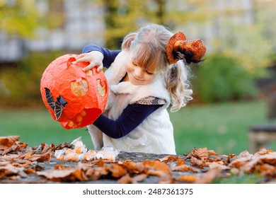 Little toddler girl dressed as a witch trick or treating on Halloween. Happy child outdoors, with orange funny hat and pumpkin bag for sweet haunt. Family festival season in october. Outdoor activity - Powered by Shutterstock