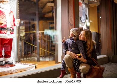 Little toddler girl with mother on Christmas market. Funny happy kid making window shopping with  Santa Claus. holidays, christmas, childhood and people concept