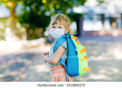 Little toddler girl on her first day on way to playschool with medical mask against corona covid virus. Healthy beautiful baby walking to nursery preschool and kindergarten. Happy child with backpack