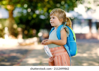 Little toddler girl on her first day on way to playschool with medical mask against corona covid virus. Healthy beautiful baby walking to nursery preschool and kindergarten. Happy child with backpack
