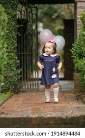 Little Toddler Girl With Pink Birthday Balloons Outside Near An Iron Fence