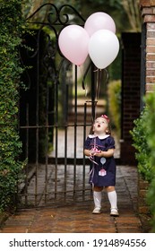 Little Toddler Girl With Pink Birthday Balloons Outside Near An Iron Fence