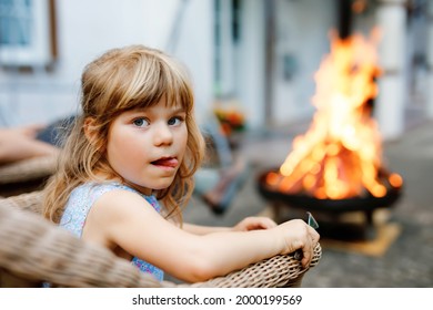 Little Toddler Girl Girl Roasting Marshmallows On Stick At Bonfire. Child Having Fun At Camp Fire. Camping With Children On Backyard. Family Leisure With Kids At Summer