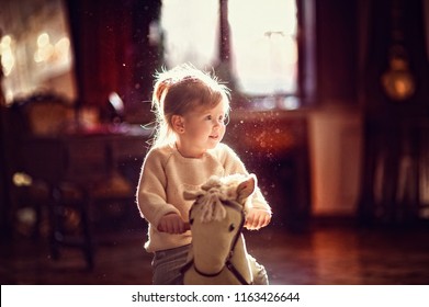 Little toddler girl sitting on toy horse before backlight from window. Happy smiling child playing at home - Powered by Shutterstock