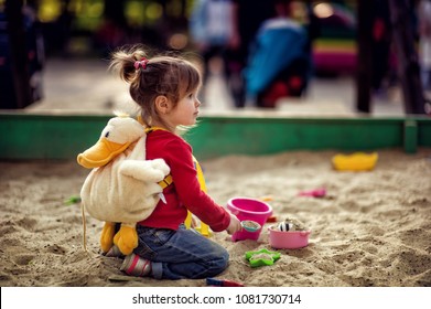 Little Toddler Girl Sitting And Playing In Sandbox Outdoors In Park. Active Child. People Concept.