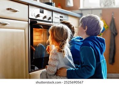 Little toddler girl and two kids boys baking pumpkin cake or cookies in kitchen. Three children, siblings, brothers and sister sitting near oven and waiting. On thanksgiving or christmas holiday. - Powered by Shutterstock