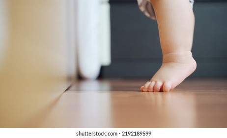 Little toddler learning to stand on the wooden floor, Baby feet. - Shutterstock ID 2192189599