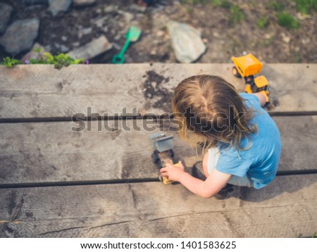 A little toddler is playing with trucks on some scaffolding planks in the garden