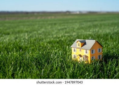 Little toy model yellow house in he middle of large grass meadow field. Horizon line and sky. Miniature, scale, downsize, mortgage payment, big yard, tiny, small, 
