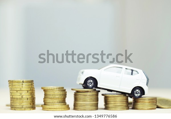Little toy white car\
over a lot of money stacked coins. for  bank loans costs finance.\
insurance, buying car finance concept. buy and pay by installments\
down payment a car.