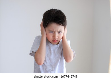 Little Trouble Boy Covered His Ear By Hand With Angry Or Mad Face On White Background. Portrait Of Mixed Race Asian-German School Kid.