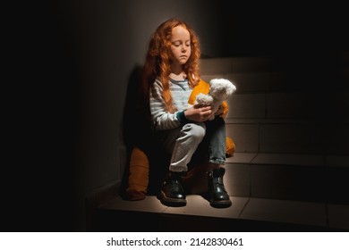 A Little Ukrainian, Sad, Curly-haired Girl Sits In The Dark On The Stairs With A Teddy Bear. She Is From Odessa
