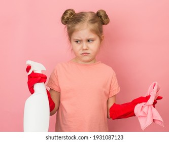 Little Unhappy Girl In Pink T-shirt And Red Gum Gloves Holding Cleaning Spray Portrait. Funny Unmotivated Cleaning Girl Making Face During Spring Cleaning At Home. 