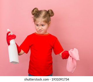 Little Unhappy Girl In Red T-shirt And Red Gum Gloves Holding Cleaning Spray Portrait On Pink Background. Funny Unmotivated Cleaning Girl During Spring Cleaning At Home. 