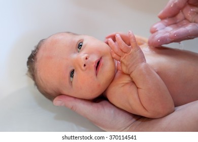 Ein kleines, sehr süßes, neu geborenes Mädchen erhält ein warmes Bad von einem Erwachsenen