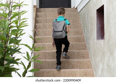 Little white Caucasian European school boy (child) comes back from school, goes upstairs to entrance door,carries schoolbag on back. Arriving to home. Independence, adolescence. Back view. Horizontal. - Powered by Shutterstock