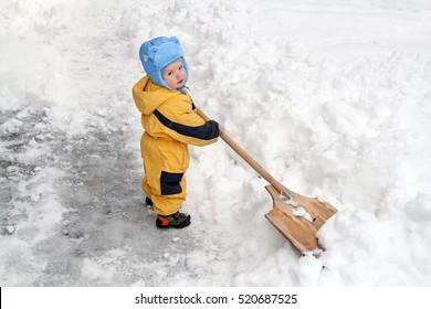 Little White Toddler with a huge shovel as a snowblower clearing snow from the road. Strong cyclone caused heavy rainfall and snow. - Powered by Shutterstock