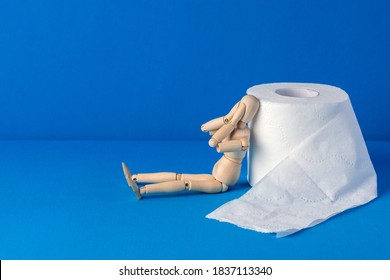 The little wooden man sits next to toilet paper and covers his face with his hands in shame and pain. Bowel problems, incontinence and diarrhea concept.