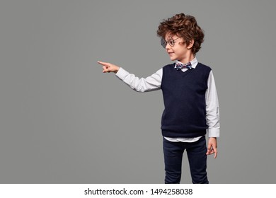 Little wunderkind in nerdy glasses smiling and pointing at empty space against gray background - Shutterstock ID 1494258038