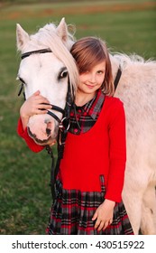 Little young girl child hugging a white pony at his head and smiling Outdoors