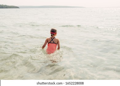 Little Young Girl Swimming In Lake River With Underwater Goggles. Child Diving In Water On Beach. Authentic Real Lifestyle Happy Childhood. Summer Fun Seasonal Outdoor Activity. View From Back.