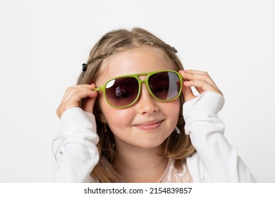 Little Young Teen Girl, Posing Mischievously In The Studio. The Background Is White And She Has Green Sunglasses That Are Really Too Big For Her.