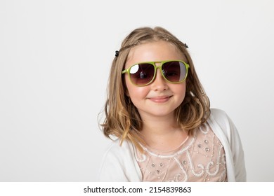 Little Young Teen Girl, Posing Mischievously In The Studio. The Background Is White And She Has Green Sunglasses That Are Really Too Big For Her.