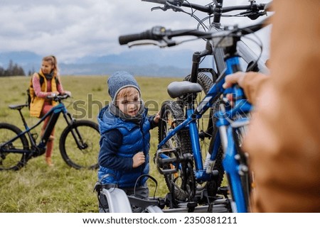 Littlle boy helping father attache a bicycle on bike carrier.