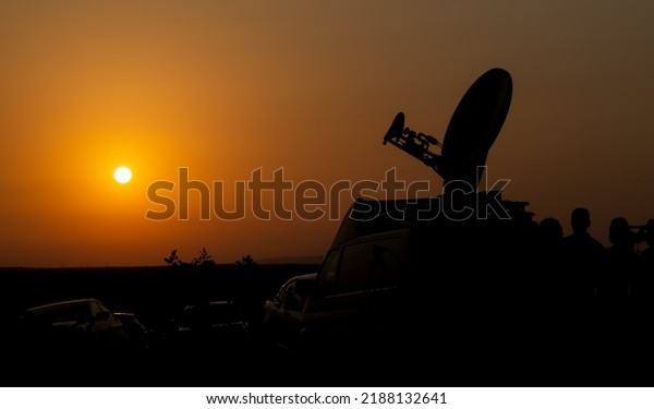 Live broadcast satellite antenna silhouette on an\
impressive summer sunset background. A live broadcast van and a\
satellite dish on it.