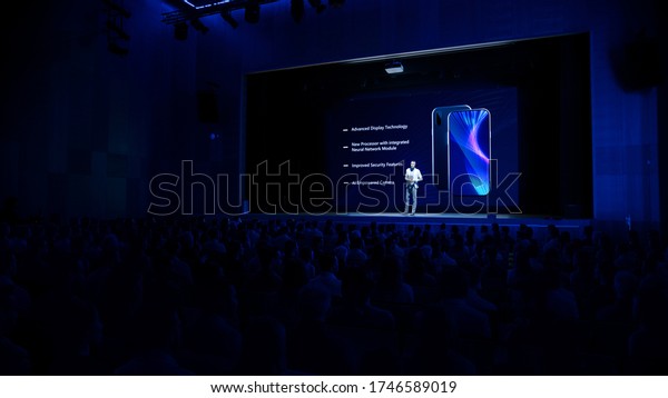 Live Event with Brand New Products Reveal:\
Keynote Speaker Presents Smartphone Device to Audience. Movie\
Theater Screen Shows Mock-up Touch Screen Phone with High-Tech\
Features and Top\
Highlights