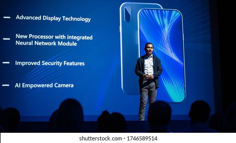Live Event with New Products Reveal: Keynote Speaker Presents Smartphone Device to Audience. Movie Theater Screen Shows Mock-up Touch Screen Mobile Phone with High End Features and Top Highlights