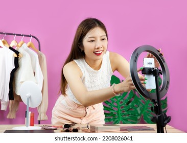 Live streaming concept, young pretty asian woman long hair beauty blogger set up smartphone camera to record video and  live chat on pink color background.