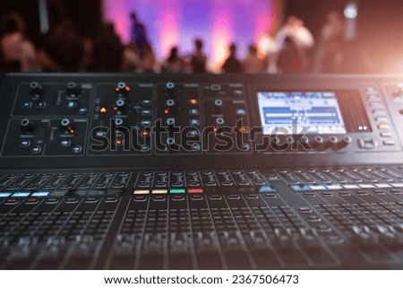 Live theater concert show sound video music control console with scene lights background. Sound engineer mixer soundboard equipment with many knobs, buttons, faders, equalizer screen and light