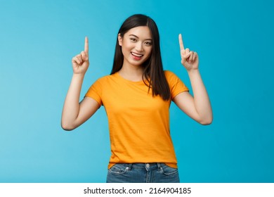 Lively asian girl dark short haircut, tilt head cute smile camera, raise hands and pointing index fingers up, introduce top promo, grinning, bragging new cool purchase, stand blue background - Shutterstock ID 2164904185
