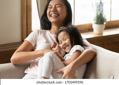 Lively Asian Young Mother Tickling Little Daughter Enjoy Free Time Active Weekend Together, Wearing Casual Comfortable Home Clothes Kid Girl Tiara Accessory, Beautiful Happy Family Having Fun Concept