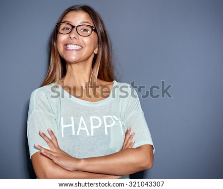 Lively attractive young Asian woman wearing glasses with a big cheesy grin standing with folded arms smiling at the camera, over grey