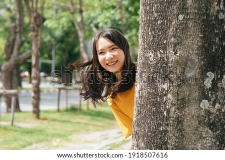 Lively brunette girl hind behind the tree and smile to the camera.
