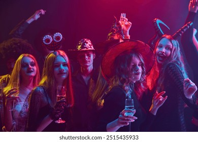 Lively group of friends, men and women attending Halloween party, dressed in various costumes of supernatural character, laughing and dancing under colorful lights in nightclub. Concept of Halloween - Powered by Shutterstock